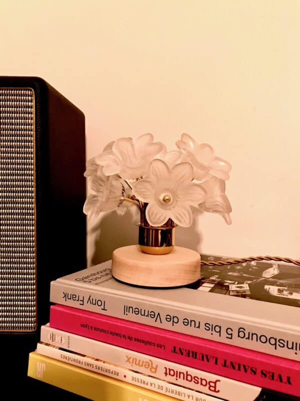 Lampe à poser en forme de petit bouquet avec 10 fleurs en verre dépoli et laiton, posée sur une pile de livres. Le socle rond est en bois massif naturel et le cordon électrique torsadé est en textile satiné couleur vieil or.