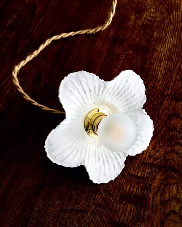 lampe baladeuse fleur blanche striée en papier mâché, avec cordon électrique torsadé en jute naturel, posée sur une table en bois.