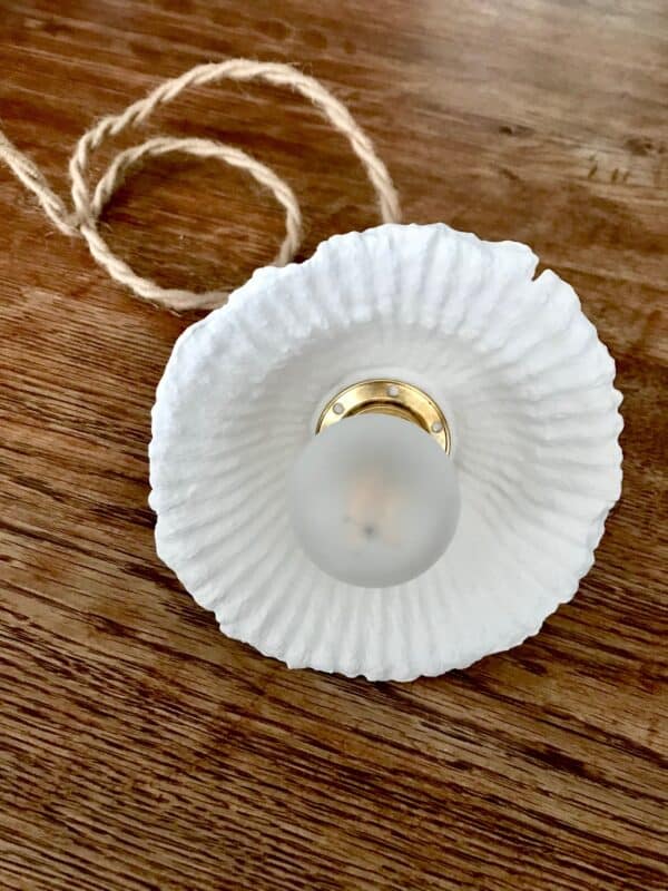 lampe baladeuse ronde blanche striée en papier mâché, avec cordon électrique torsadé en jute naturel, posée sur une table en bois.