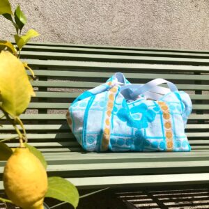 Cabas en tissu éponge motif fleurs, bleu, posé sur un banc au soleil à côté d'un citronnier.