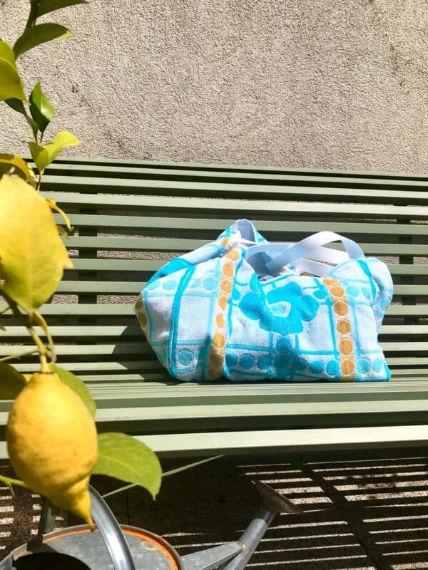 Cabas en tissu éponge motif fleurs, bleu, posé sur un banc au soleil à côté d'un citronnier.