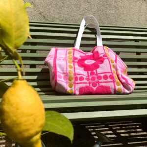 Cabas en tissu éponge motif fleurs, rose, posé sur un banc au soleil à côté d'un citronnier.