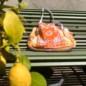 Cabas en tissu éponge motif fleurs, orange, posé sur un banc au soleil à côté d'un citronnier.
