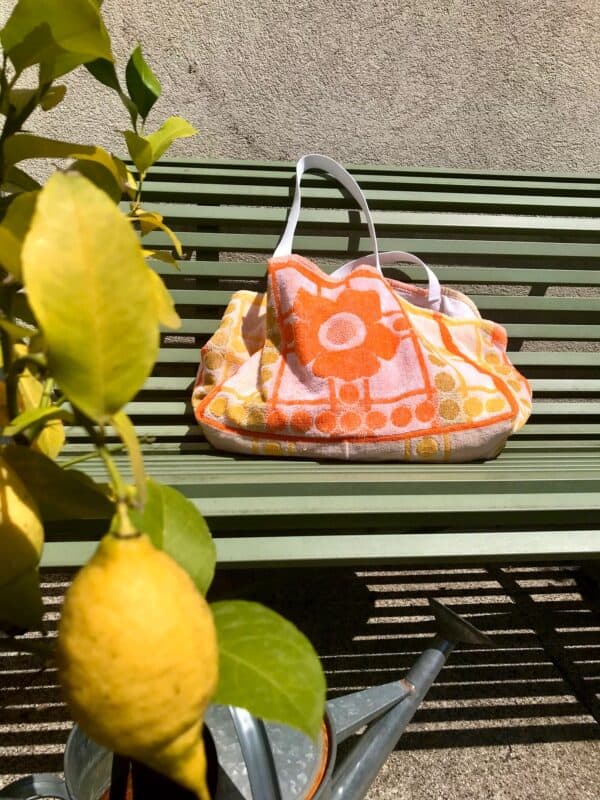 Cabas en tissu éponge motif fleurs, orange, posé sur un banc au soleil à côté d'un citronnier.